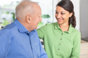 caregiver smiling while assisting elderly man