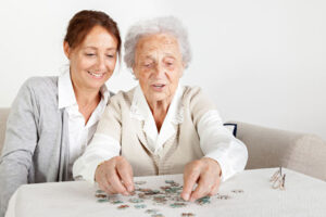 A woman works on a puzzle with her older mother because she knows that it’s important to incorporate activities that improve self-esteem in those with dementia.